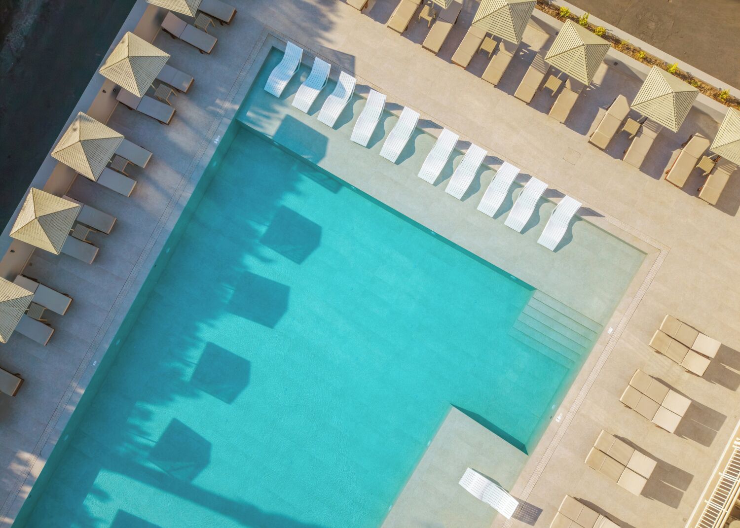 An aerial view of a rectangular swimming pool surrounded by lounge chairs and umbrellas.
