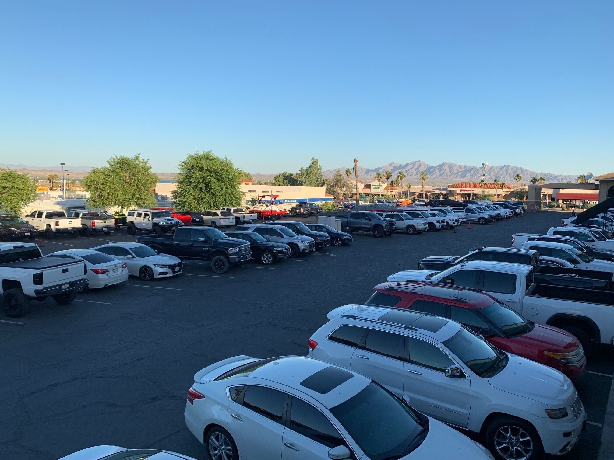 A parking lot with various vehicles, including cars and trucks, and a mountainous landscape in the background.