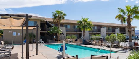 A pool area with lounge chairs and a table, surrounded by a fence and palm trees.