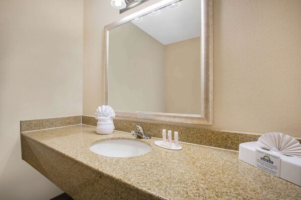 Un baño con encimera de granito, un lavabo, un espejo y una caja de pañuelos.