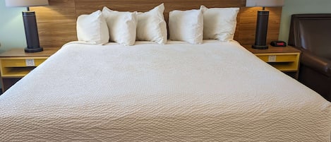 Una cama bien hecha con un edredón blanco texturizado, dos mesitas de noche con lámparas y un cabecero de madera.