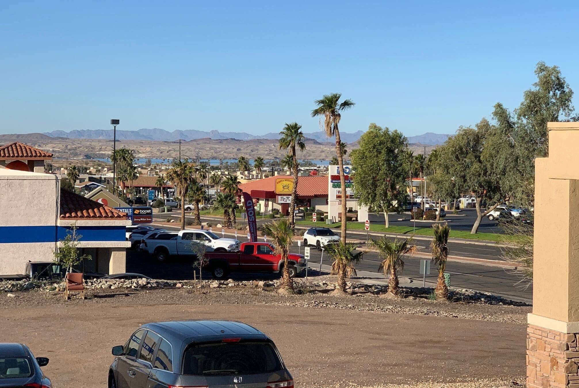 A parking lot with several cars, a building with a blue and white facade, and palm trees.