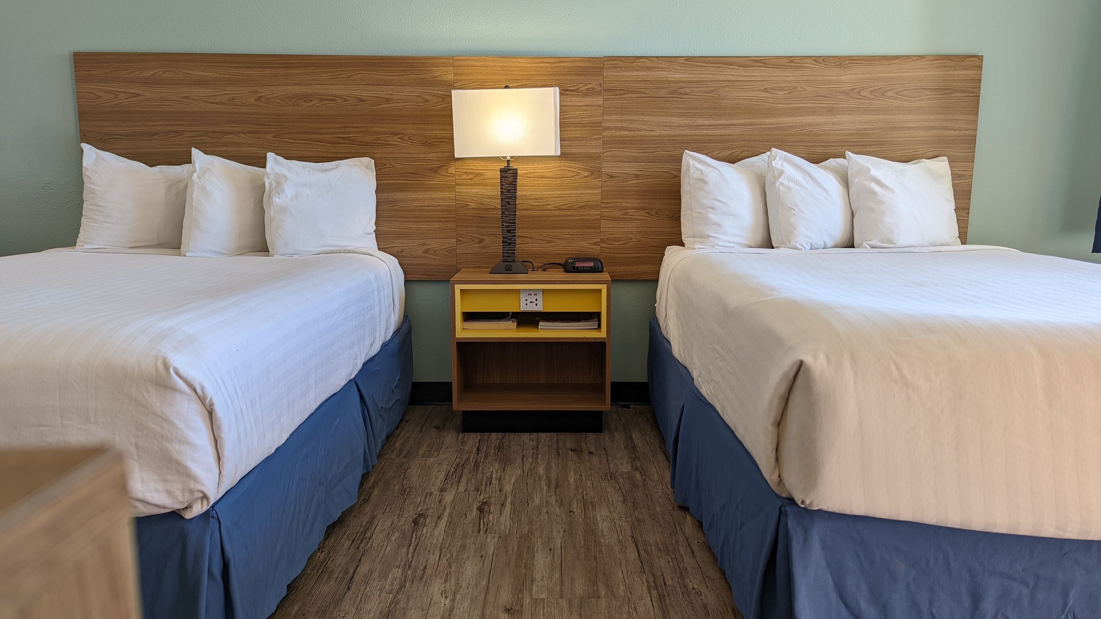 Habitación doble con dos camas, una mesita de noche con lámpara y cabecera de madera.