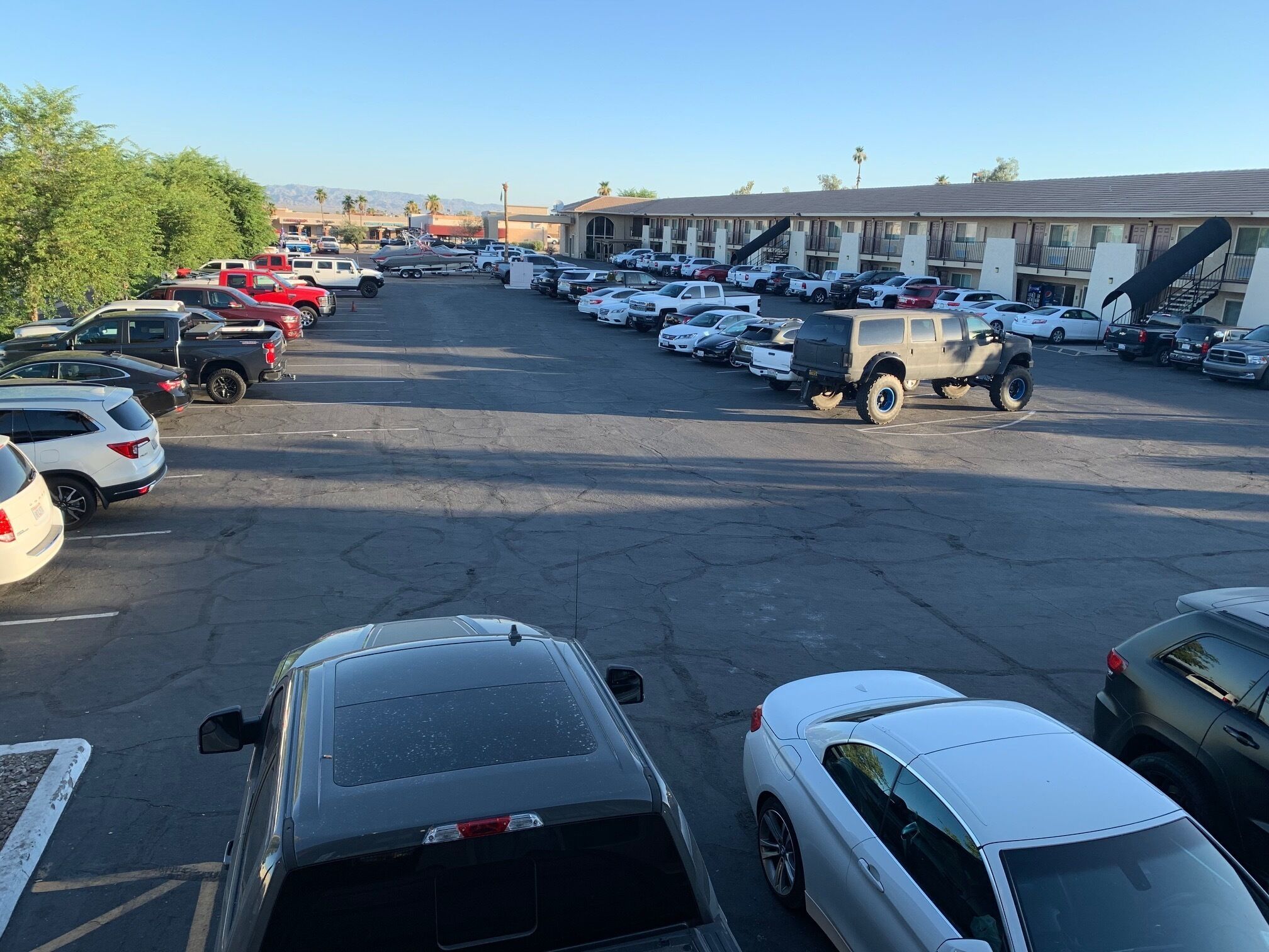 A parking lot with various vehicles, including cars and SUVs, and a building with a staircase in the background.