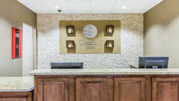 Un mostrador de recepción de hotel con un fondo de pared de piedra, un letrero que dice "Comfort Inn" y un monitor de computadora Dell.