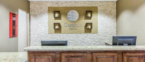 Un mostrador de recepción de hotel con un fondo de pared de piedra, un letrero que dice "Comfort Inn" y un monitor de computadora Dell.