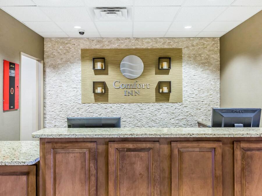 Un mostrador de recepción de hotel con un fondo de pared de piedra, un letrero que dice "Comfort Inn" y un monitor de computadora Dell.