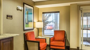 Un hall d’hôtel avec deux fauteuils orange, un bureau avec un téléphone, un tableau encadré au mur et une fenêtre donnant sur la rue.