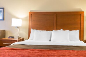 A hotel room with a wooden headboard, white bedding, a red blanket, a bedside lamp, and a clock on the nightstand.