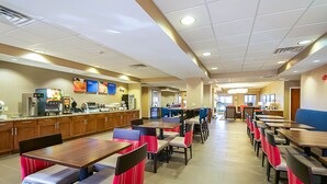 Un grand espace de salle à manger avec plusieurs tables et chaises, un coin cuisine équipé de divers appareils et un environnement propre et bien éclairé.