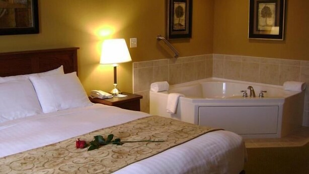A hotel room with a large bed, a bedside lamp, a bathtub, and framed pictures on the wall.