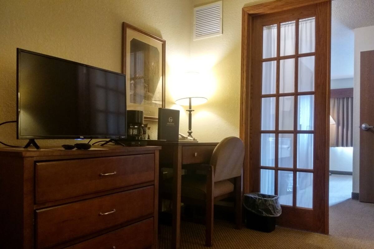 Ett hotellrum med ett skrivbord i trä, en tv, en lampa, en stol och en dörr som leder ut till en balkong.