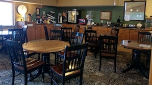A dining area with wooden tables and chairs, a clock on the wall, and a television mounted above the counter.