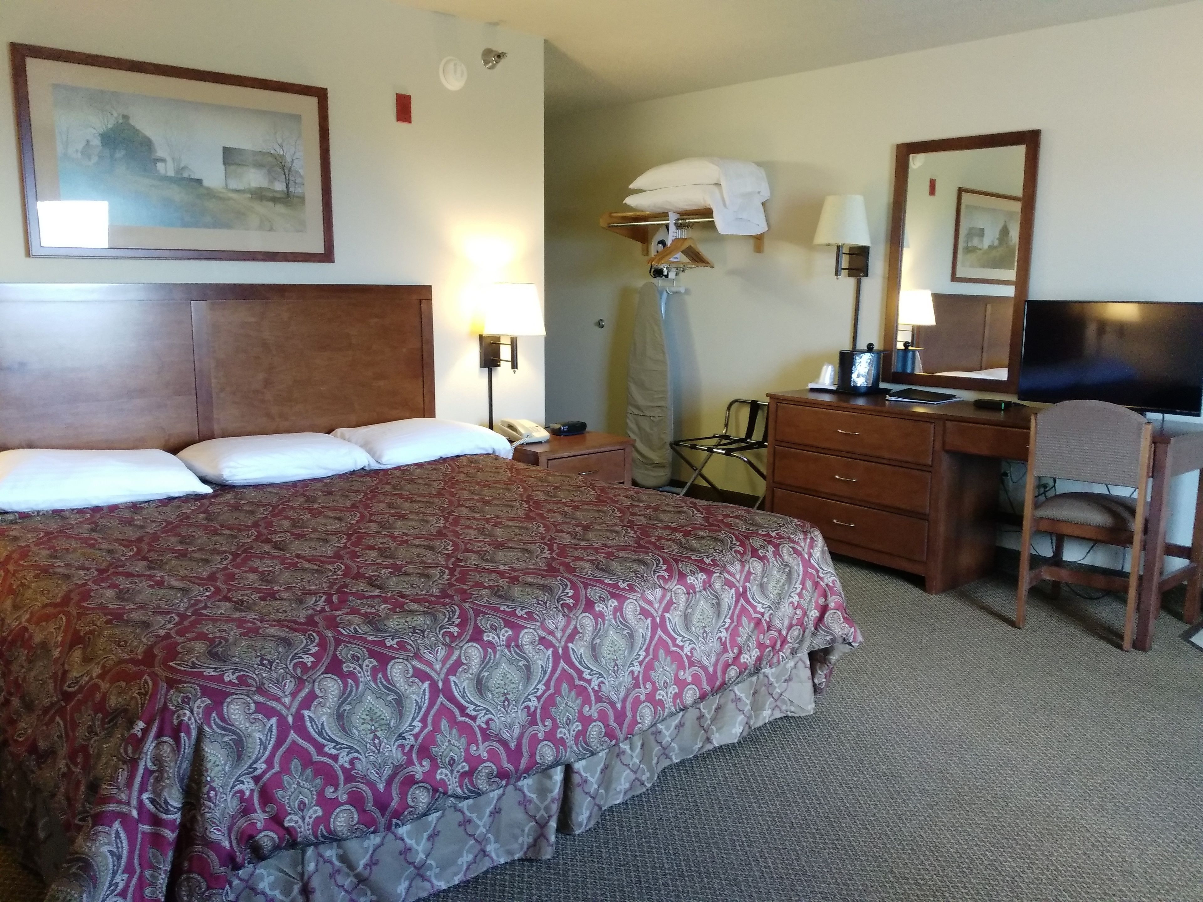 A hotel room with a large bed, a desk with a chair, a television, and a lamp.
