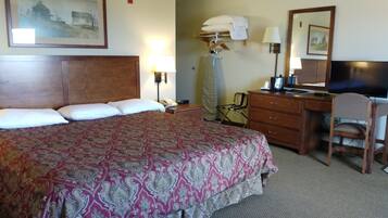 A hotel room with a large bed, a desk with a chair, a television, and a lamp.