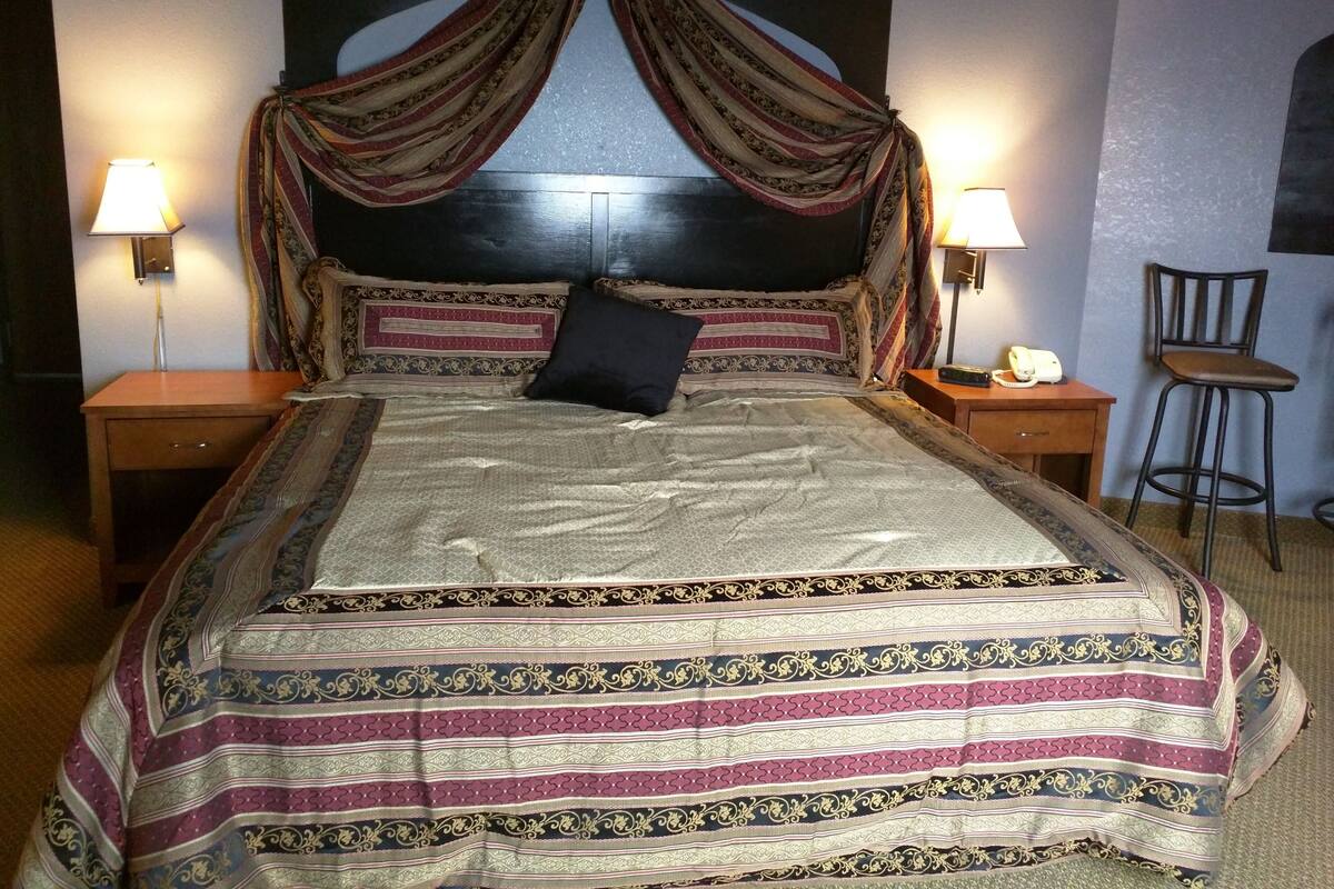 En säng med himmelssäng, två sänglampor, ett nattduksbord, en stol och en telefon som är monterad på väggen.