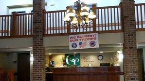 A hotel reception area with a sign stating "WE SUPPORT OUR TROOPS" and a logo for the hotel. There is a reception desk, a clock, and a chandelier above.