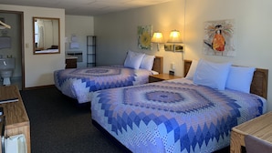 A hotel room with two beds, a desk, a chair, a mirror, a toilet, and a shower area. - Chief Motel (Custer)