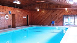 A large indoor swimming pool with wooden walls and a blue floor. There is a door and a chair visible. - Chief Motel (Custer)