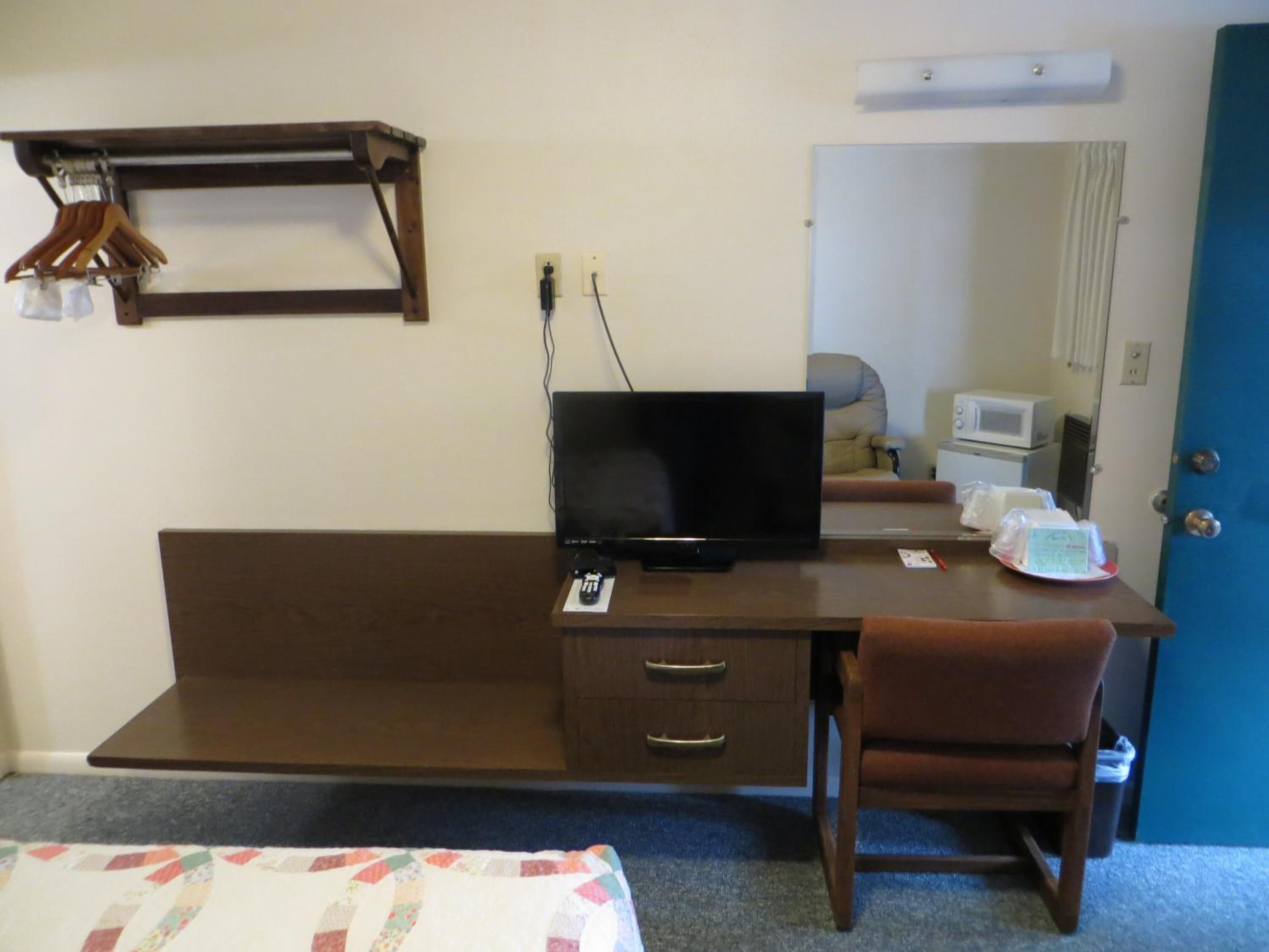 A hotel room with a wooden desk, a television, a chair, a bed, and a microwave.