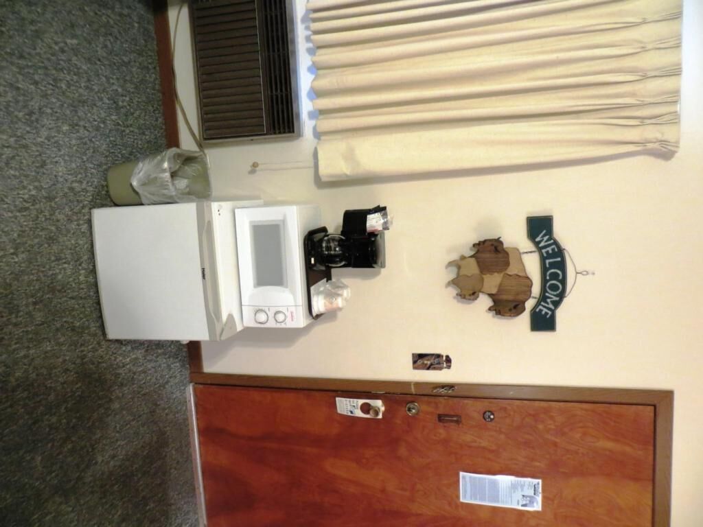 A room with a white refrigerator, a coffee maker, a 'WELCOME' sign, a wooden door, and a window with blinds.