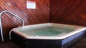 A wooden spa tub with a metal ladder, a caution sign, and a wooden floor. - Chief Motel (Custer)
