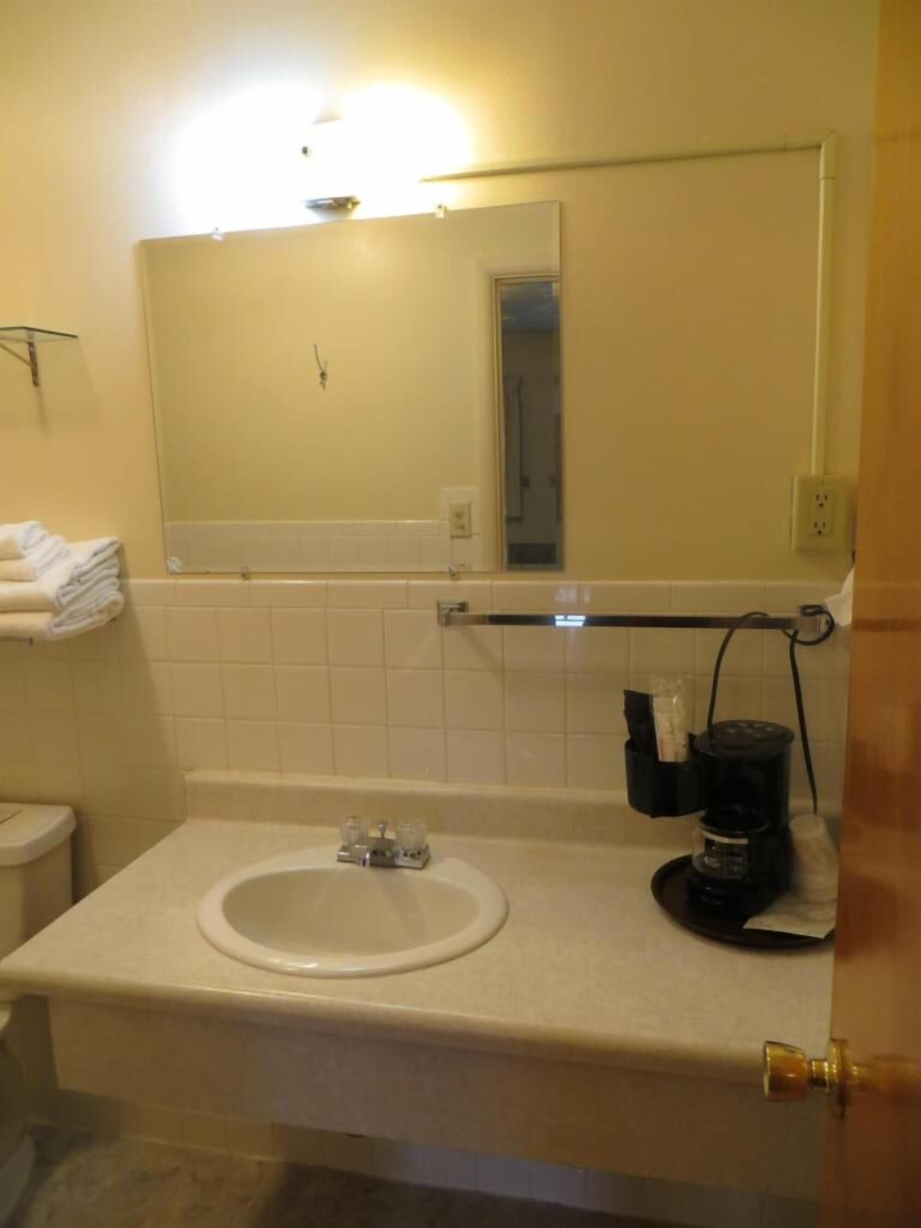 A bathroom with a white sink, a mirror, a towel rack, and a coffee maker.