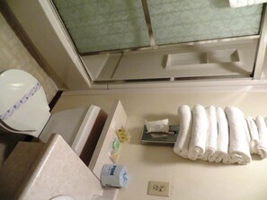 A bathroom with a toilet, a towel rack with towels, a soap dispenser, and a window with a floral pattern.