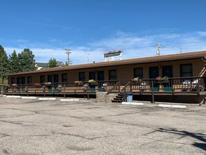 A motel with a long, single-story building, a covered parking area, and a sign indicating a tasting room and restaurant.