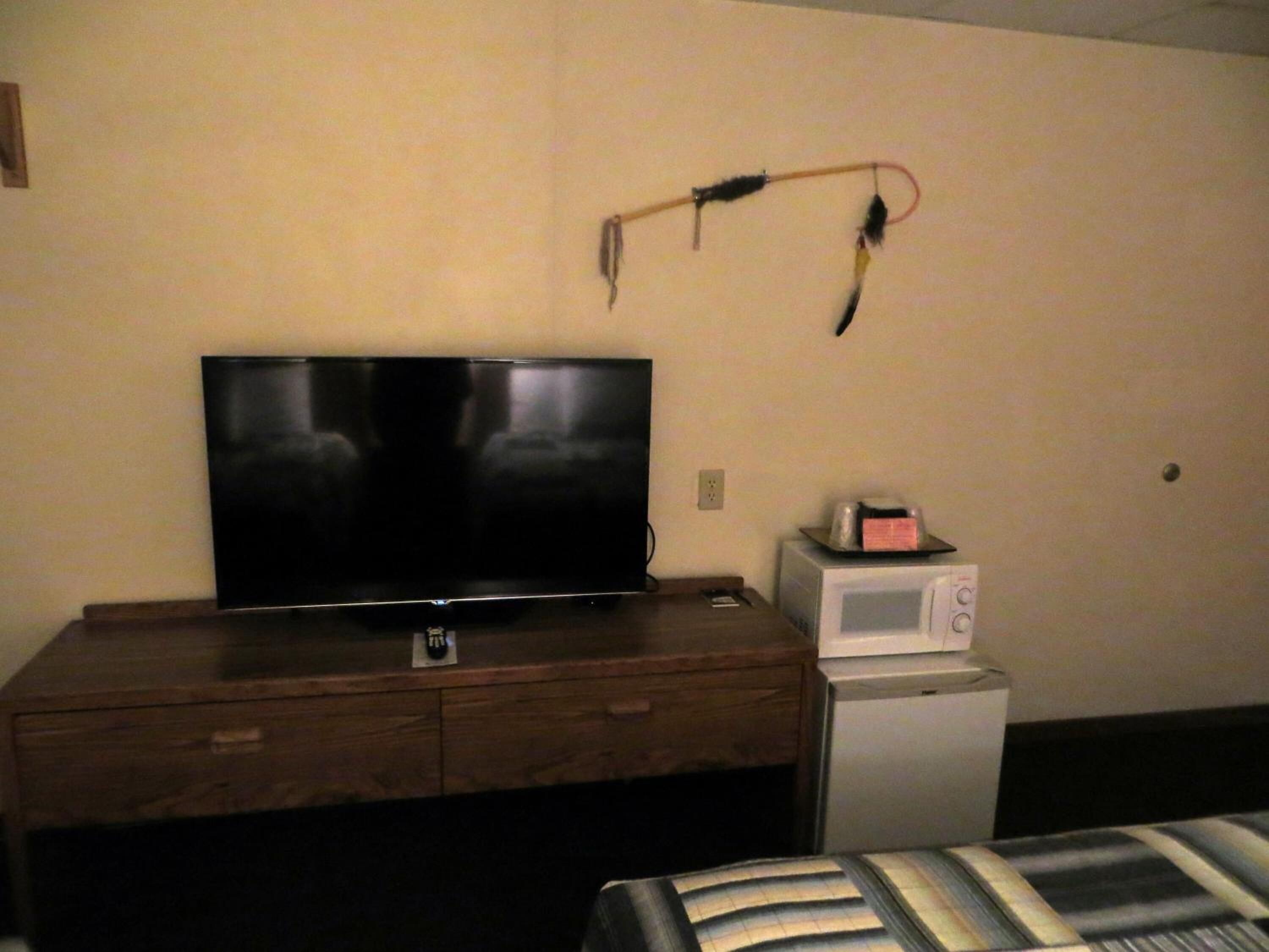 A room with a flat-screen TV on a wooden dresser, a microwave, and a power strip on the wall.