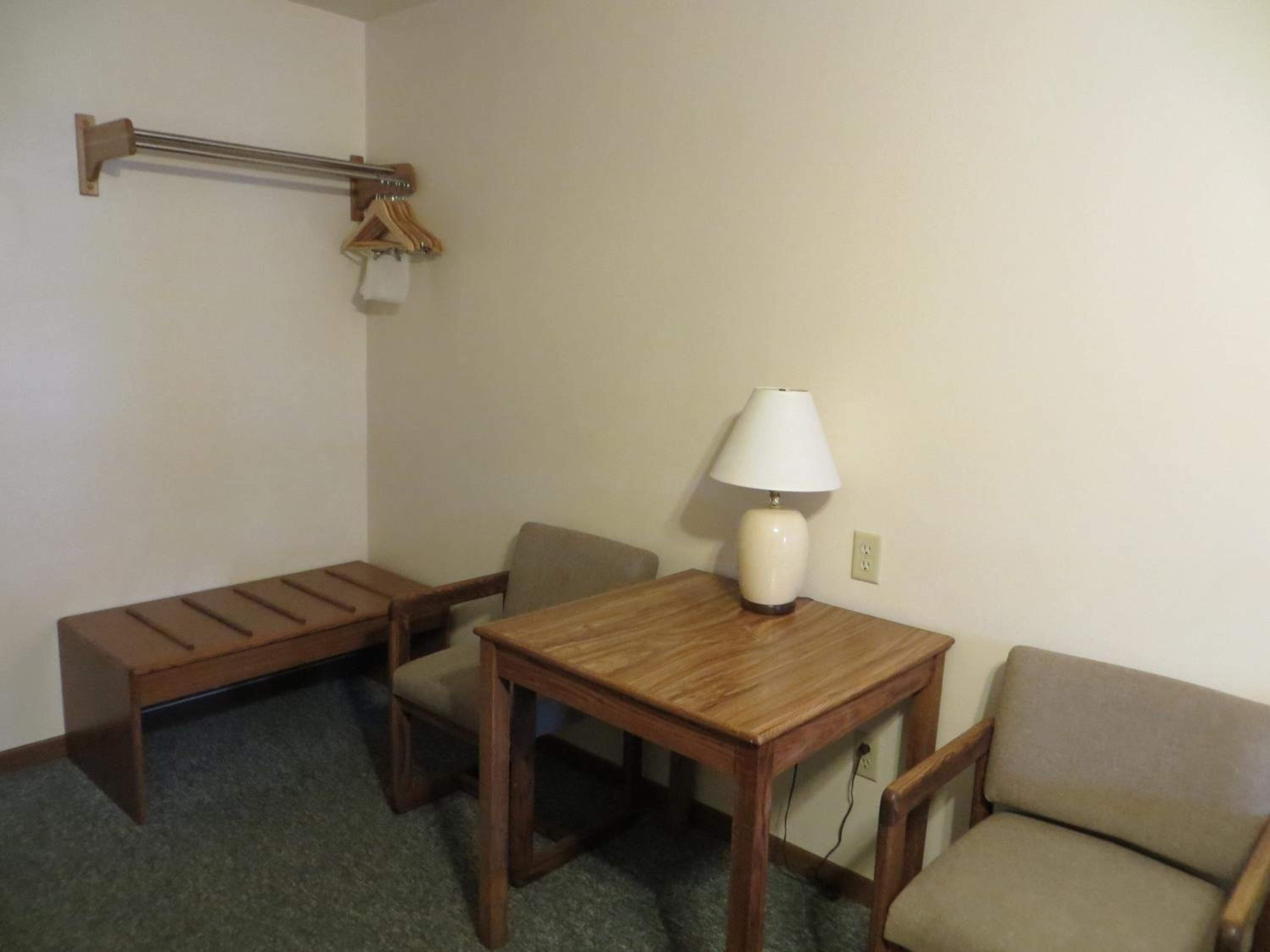 Une petite pièce simple, avec une table en bois, deux chaises, une lampe et un porte-manteau avec des cintres.