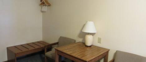 Une petite pièce simple, avec une table en bois, deux chaises, une lampe et un porte-manteau avec des cintres.