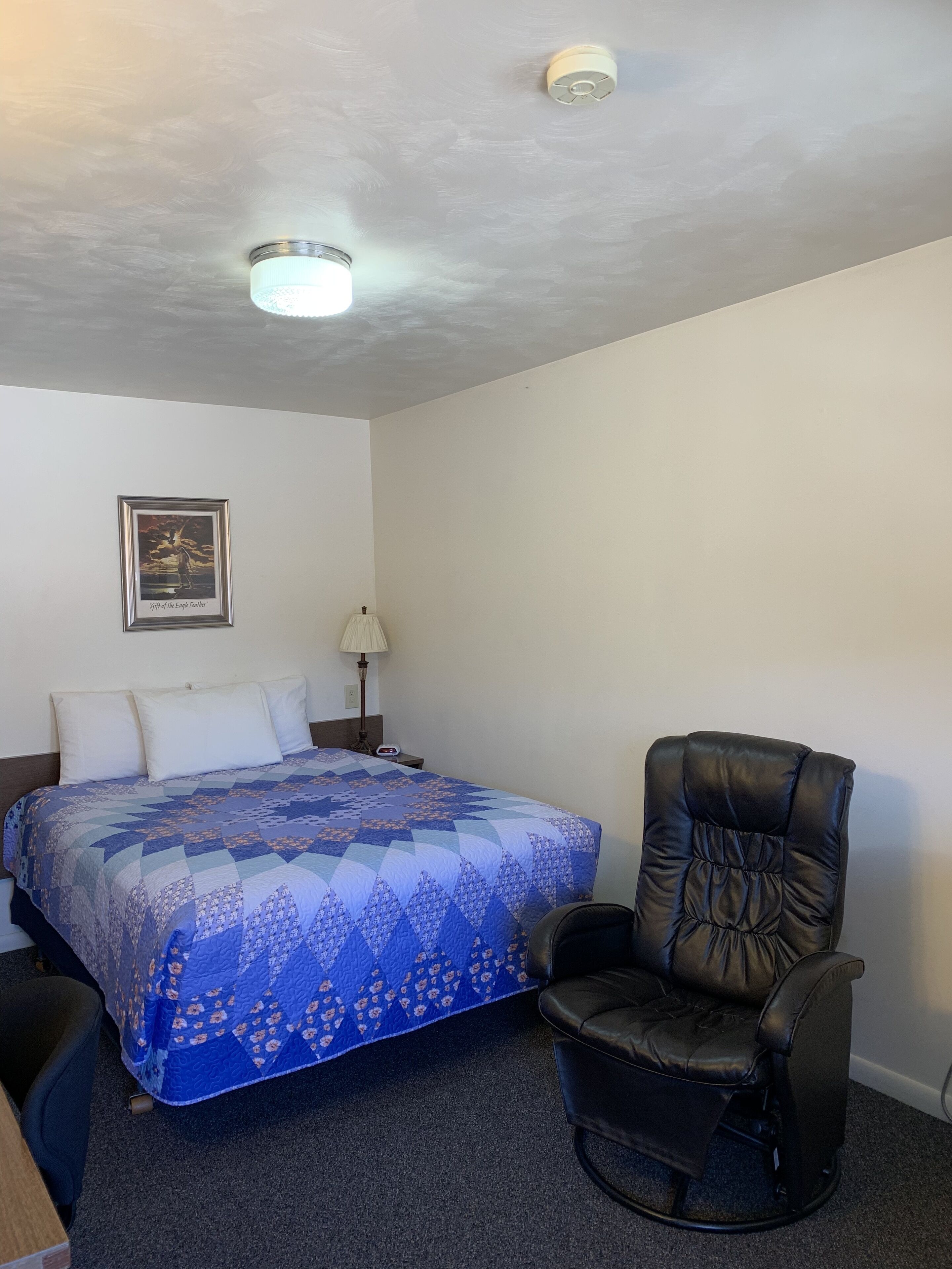 A hotel room with a bed, a chair, a lamp, and a ceiling light.