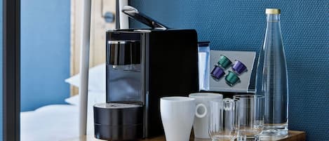 A hotel room's minibar with a coffee maker, a bottle, and some glasses.