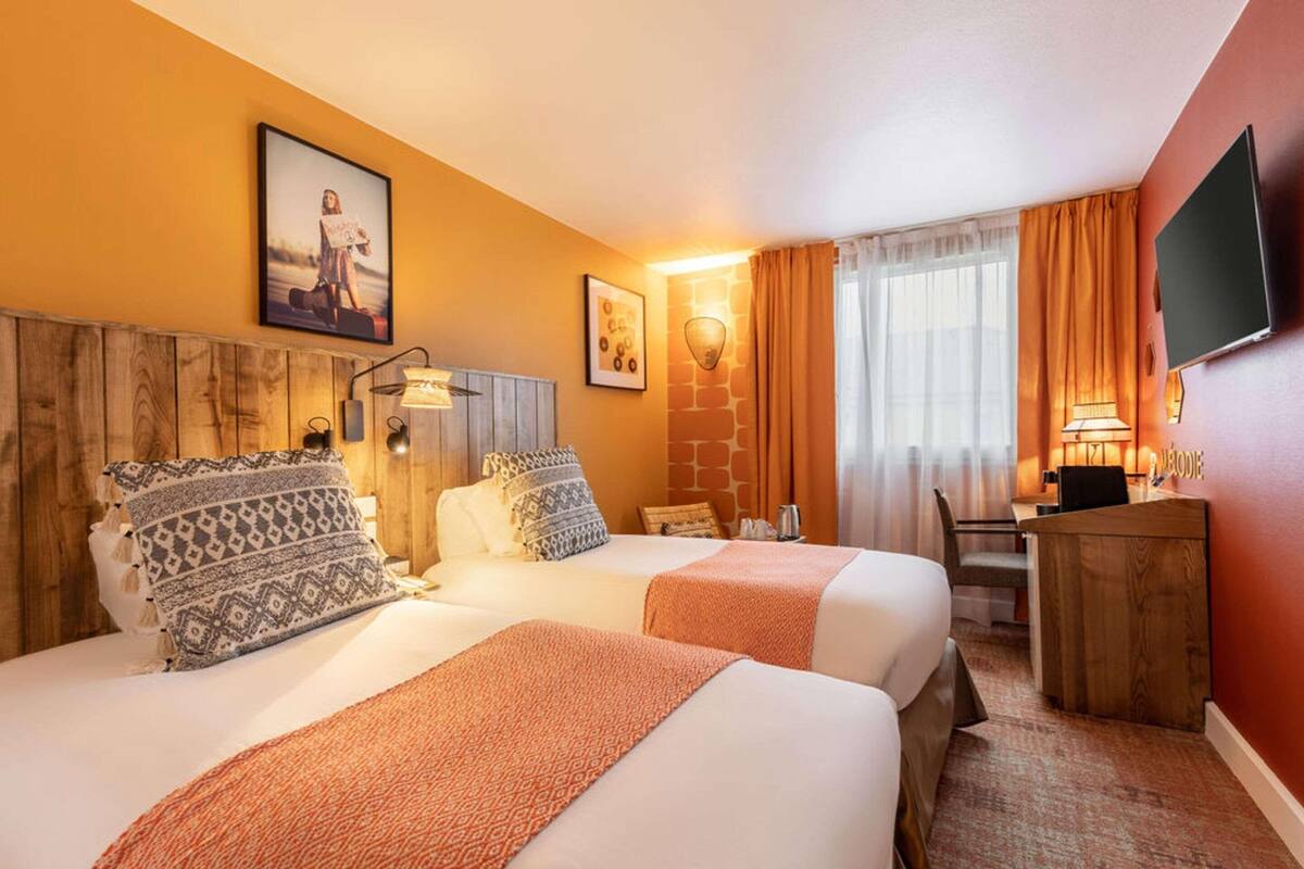 Ein Hotelzimmer mit zwei Betten, einem Schreibtisch, einem Fernseher und einer Steinwand.