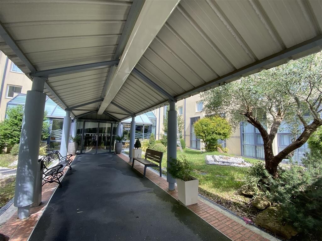 A covered walkway with benches and a grassy area with trees.
