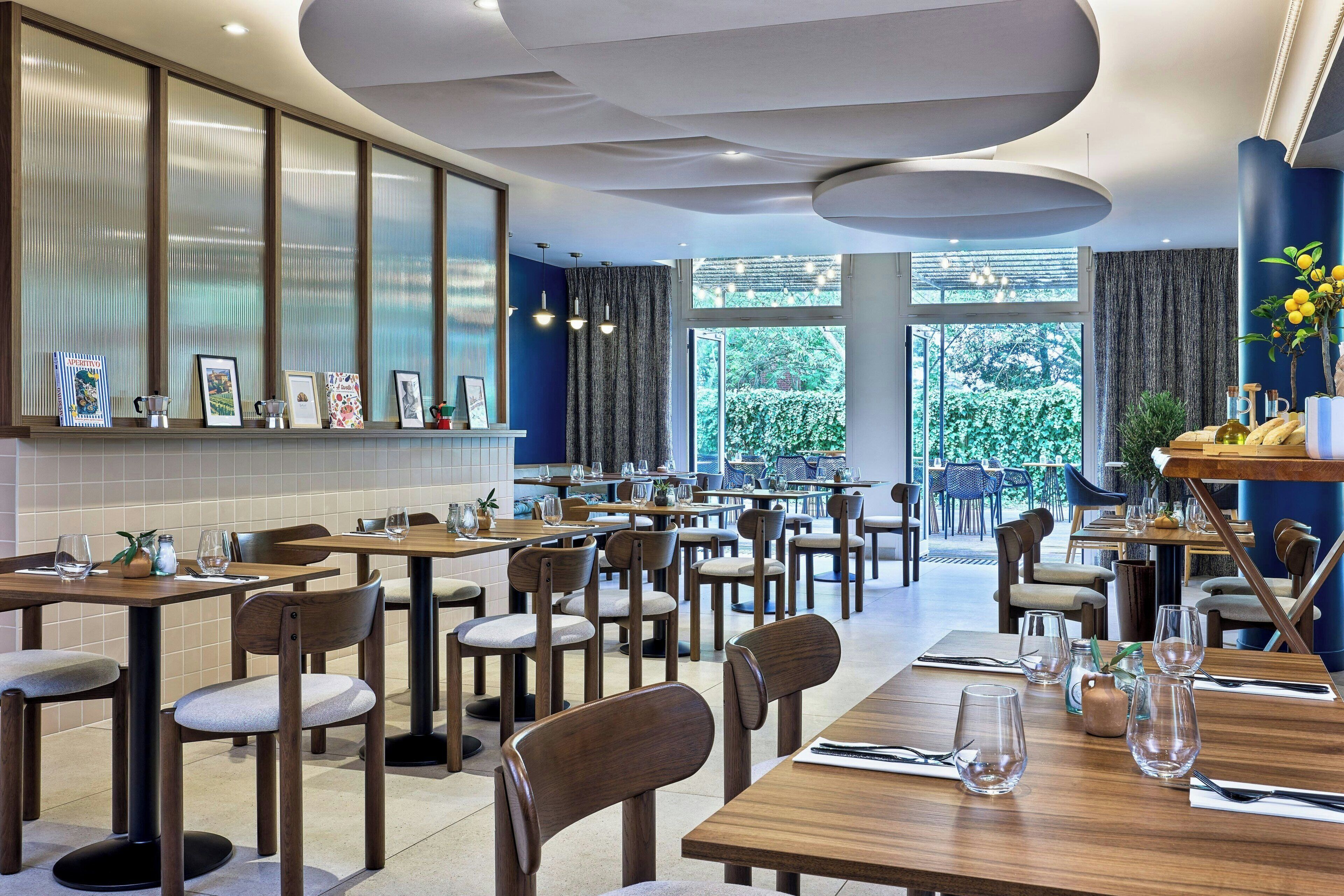 A modern restaurant interior with multiple dining tables, chairs, and a variety of framed pictures on the wall.