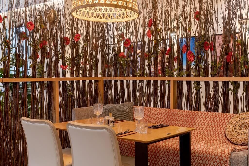 Un coin repas avec une table dressée pour deux personnes, un canapé et un mur décoratif agrémenté d’éléments verticaux.