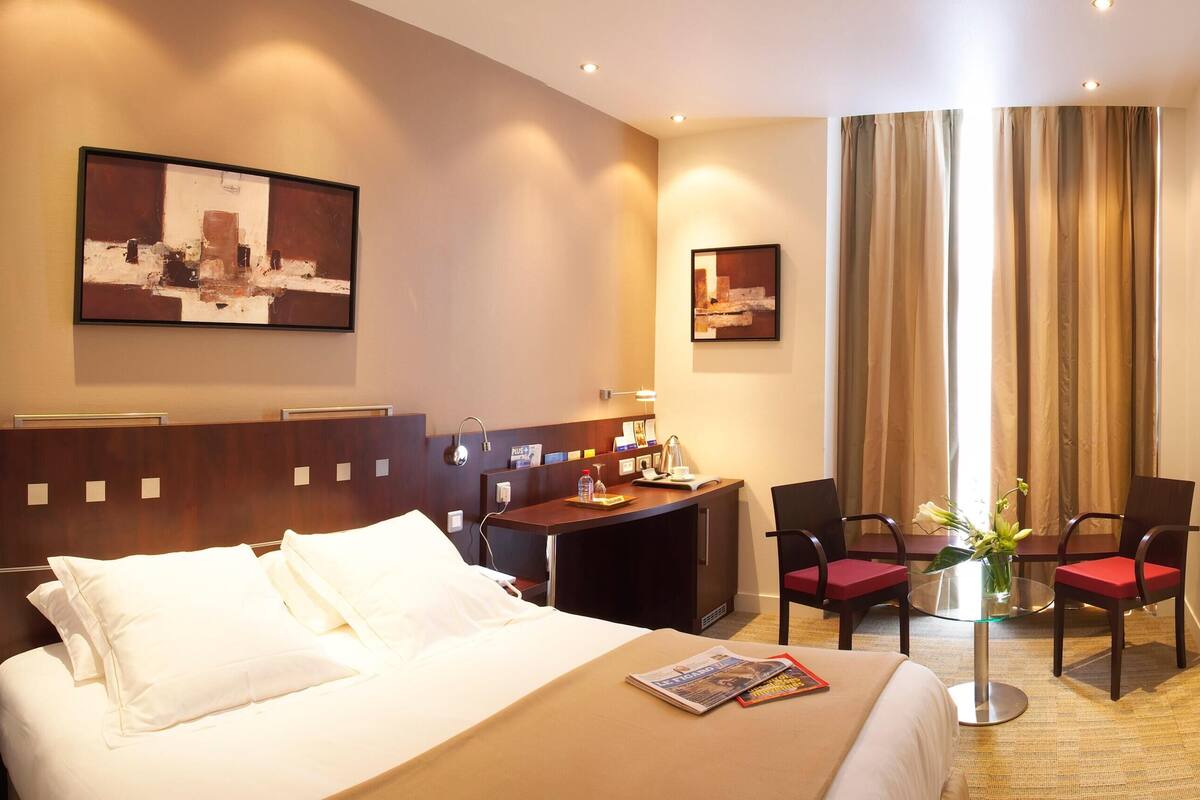 Ein Hotelzimmer mit Bett, Schreibtisch, Sesseln, Fernseher und Bildern an den Wänden.