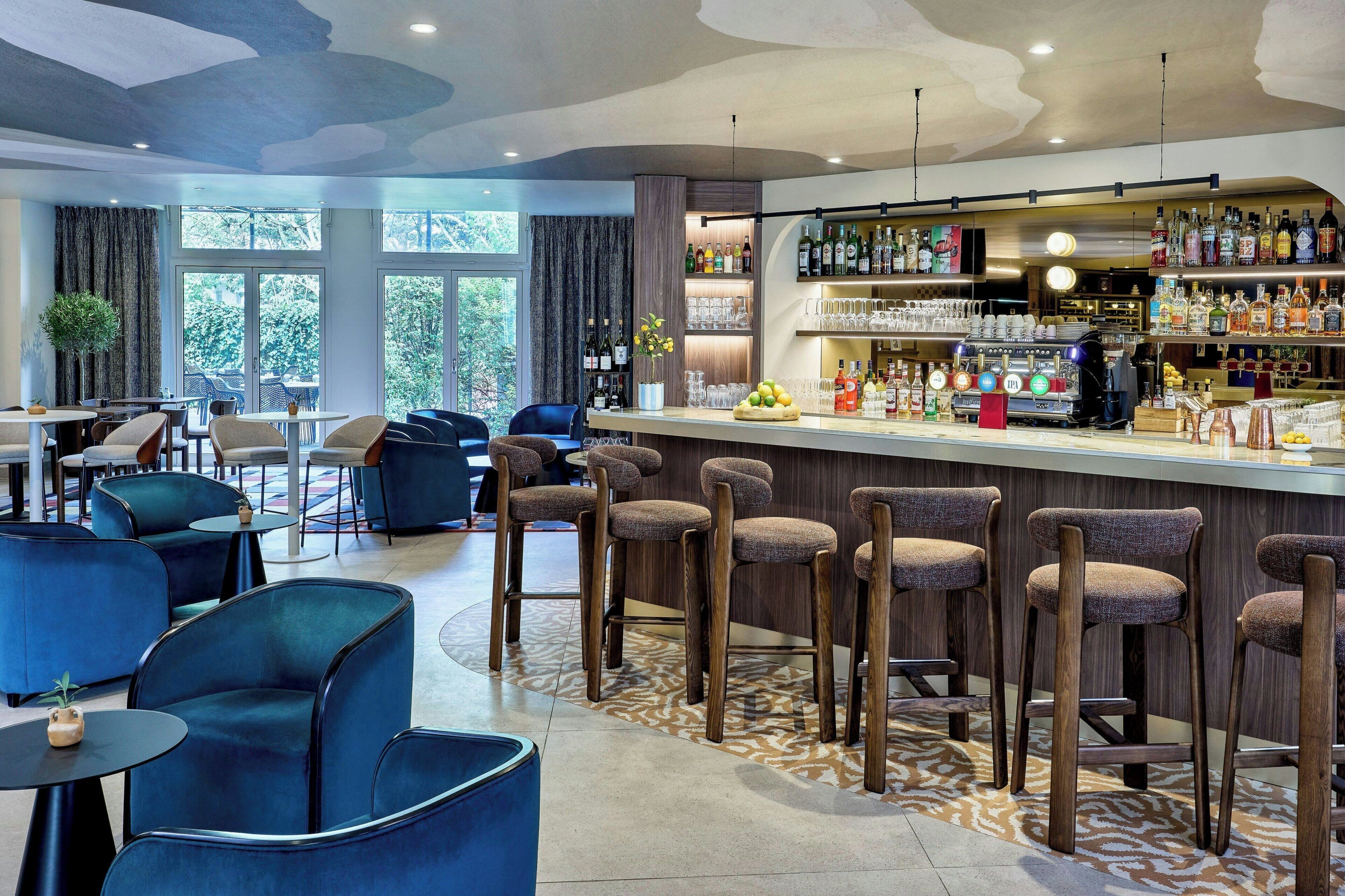 A bar area with stools, a bar counter, and a variety of bottles and glasses.