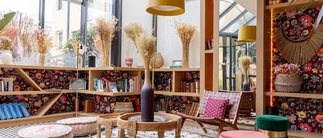 A room with a large window, a round table, and a bookshelf filled with books and decorative items.