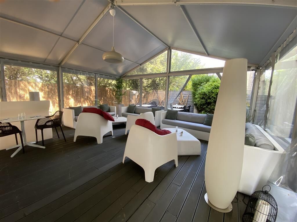 Ein überdachter Außenbereich mit weißen Möbeln und einem Tisch, umgeben von einer Holzterrasse.