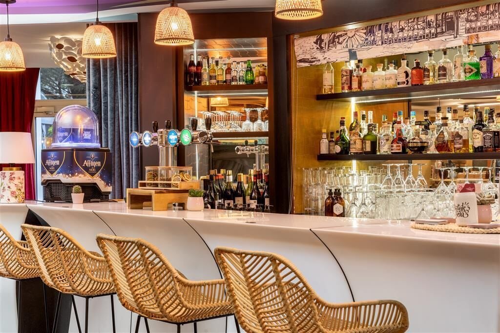 A bar area with wicker chairs, a minibar, and shelves stocked with bottles and glasses.