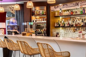 Eine Bar mit Korbstühlen, einer Minibar und Regalen voller Flaschen und Gläsern.