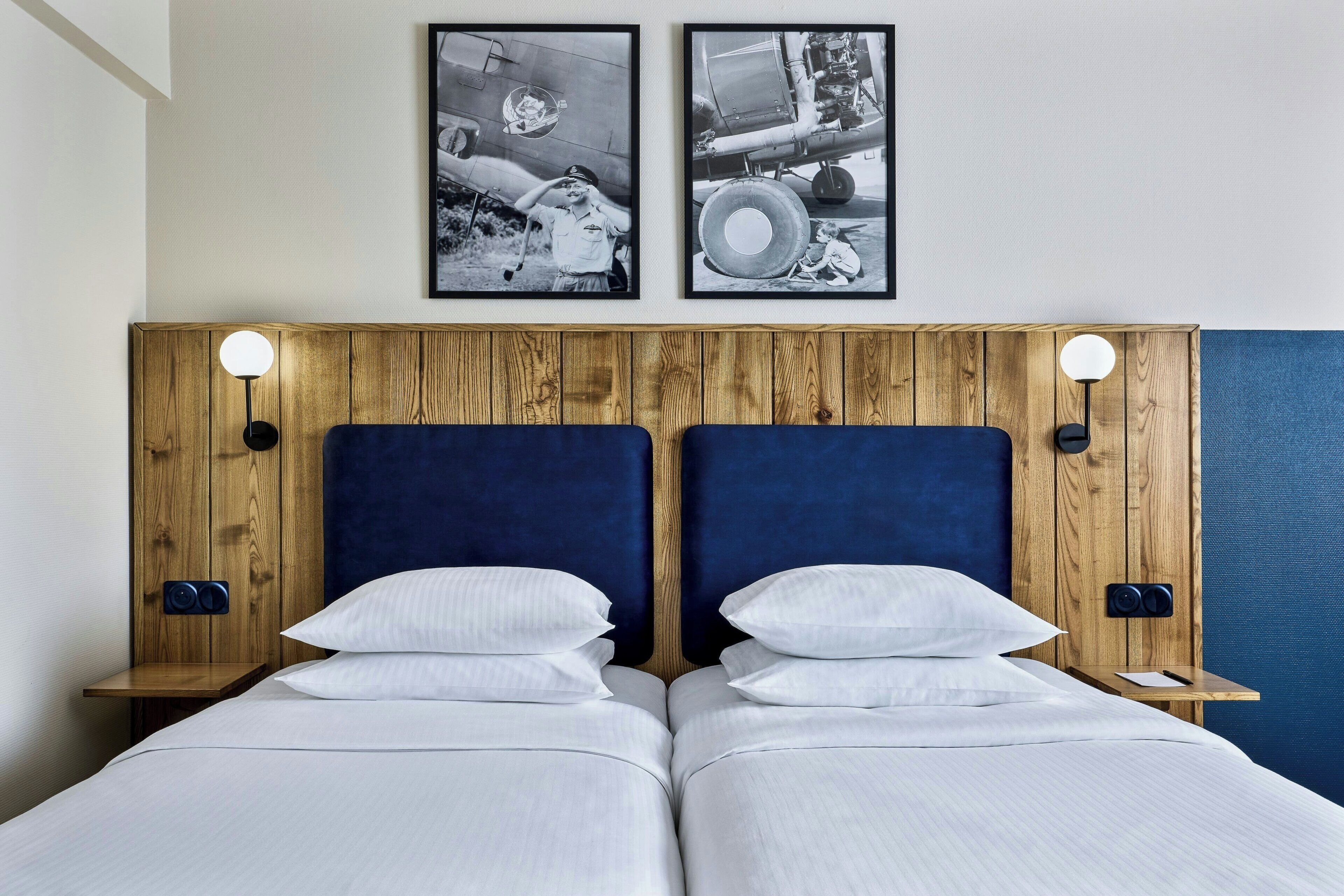 A double bed with white linens, wooden headboard, and two wall-mounted nightstands with lamps.