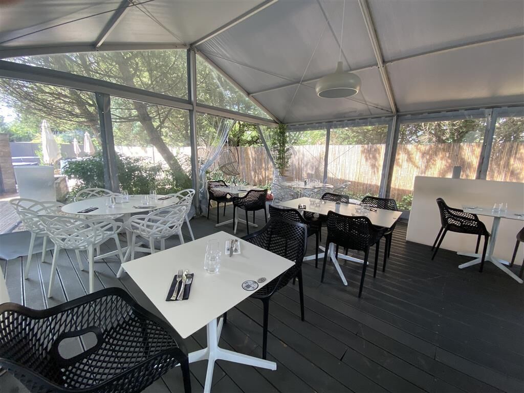 Een terras buiten met meerdere tafels en stoelen, overdekt met een transparante constructie.