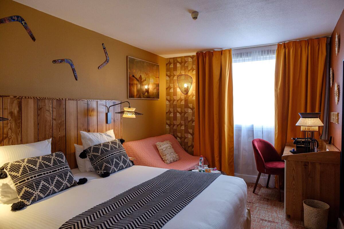 Ein Hotelzimmer mit einem großen Bett, einem Schreibtisch, einem Sessel und einem Fenster mit Vorhängen.