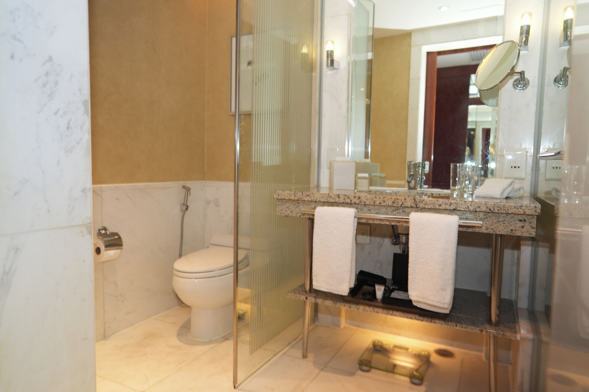 Een moderne badkamer met een douchecabine van glas, een toilet, een wastafel met spiegel en een handdoekrek.
