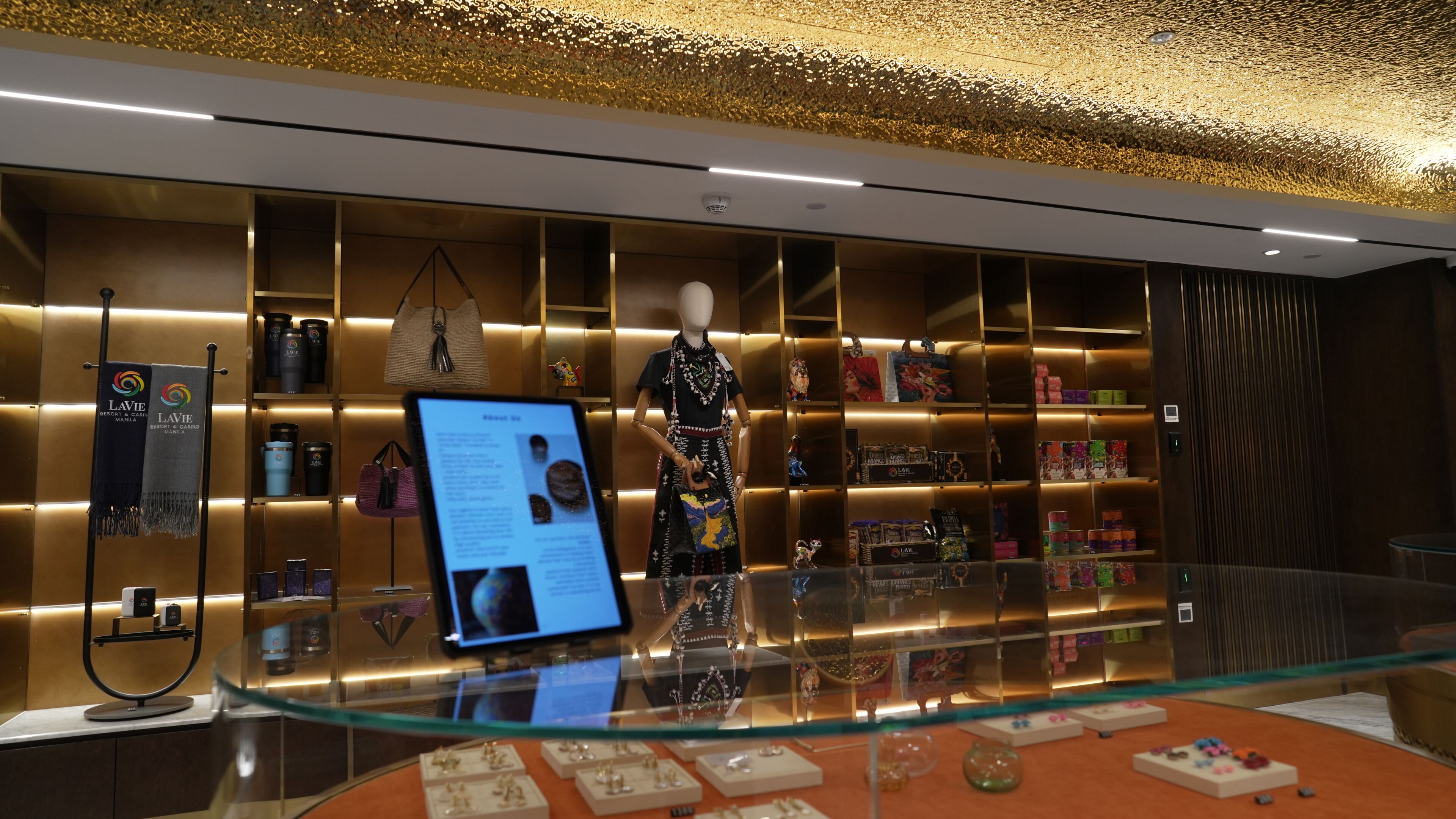 Vitrine de joias com um manequim, prateleiras com diversos itens e uma tela digital.