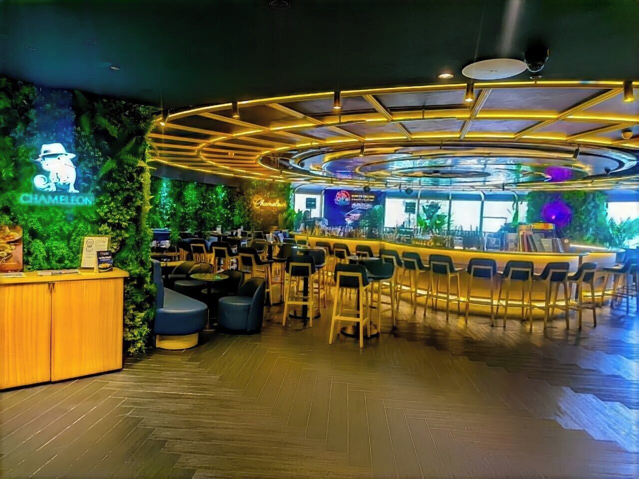 A bar area with a curved counter, seating, and a neon sign.